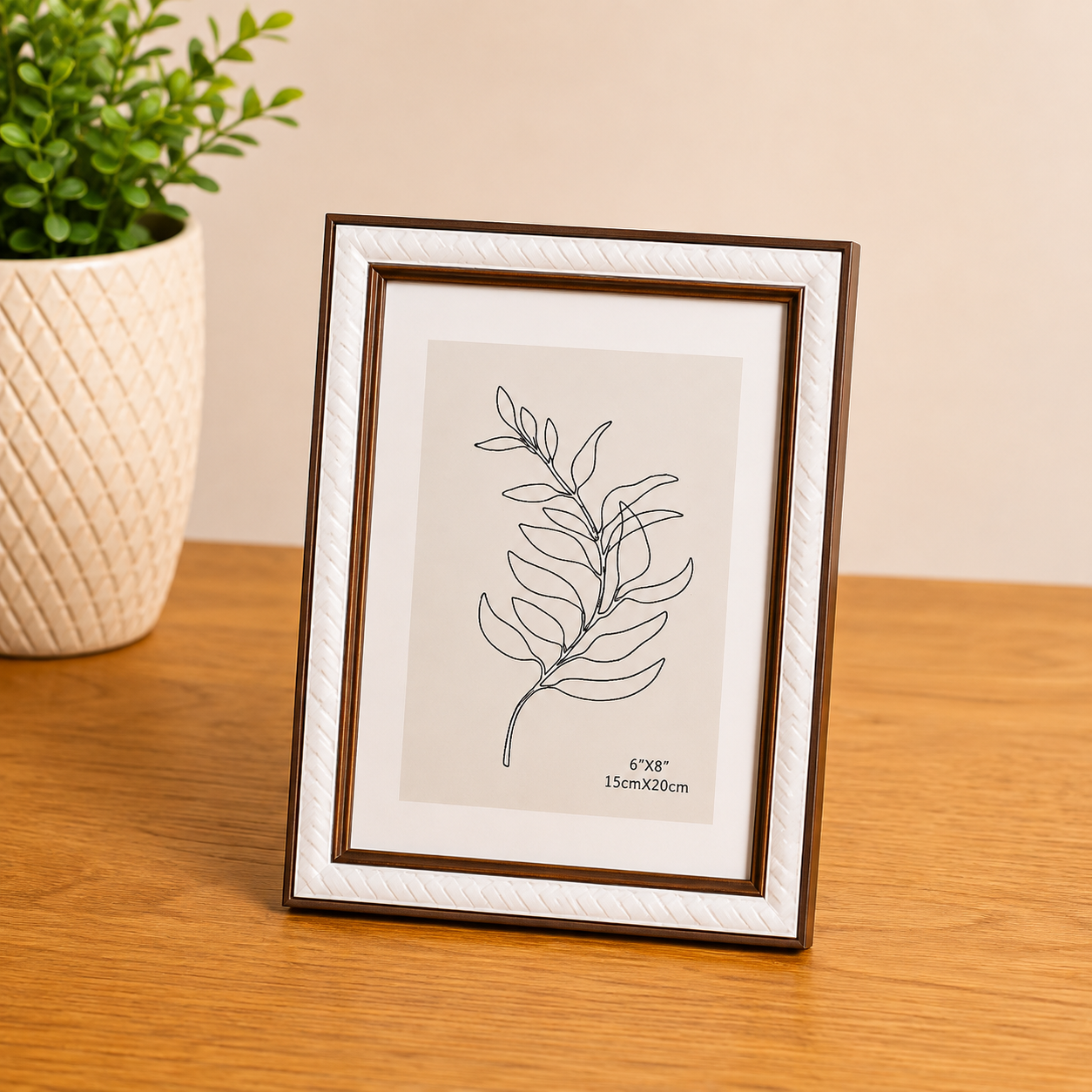 Porta retrato amadeirado e branco com ilustração de folha em fundo claro, ao lado de vaso com planta em ambiente de madeira